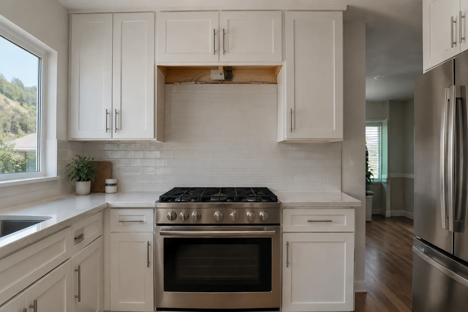 Eye-level wide view of a residential kitchen with a stainless gas range beneath a central open section of white upper cabinetry, white backsplash and counters, sink and window at left, and refrigerator at right.