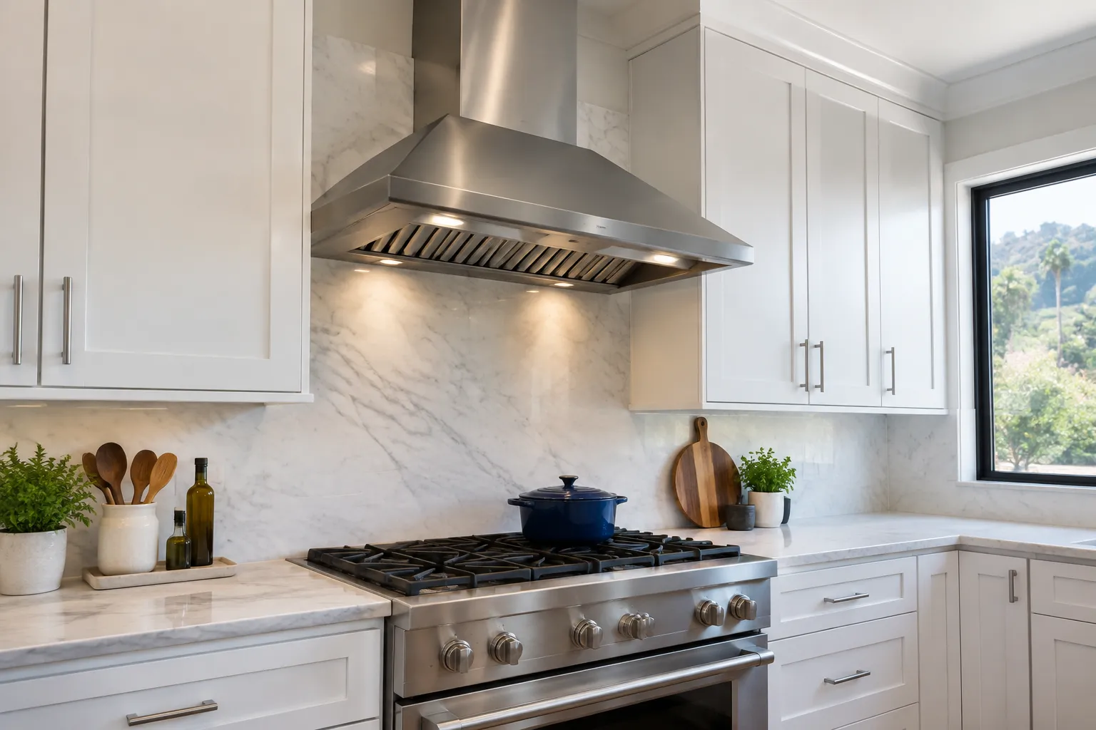 A stainless-steel range hood is installed above a six-burner gas range beneath white upper cabinets, with a visible chimney extending toward the ceiling; cookware rests on the range in a finished kitchen.